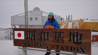 写真：昭和基地の立て看板の前で微笑む隊員